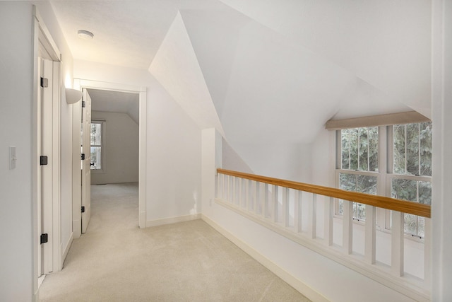 hallway with light carpet, baseboards, and lofted ceiling