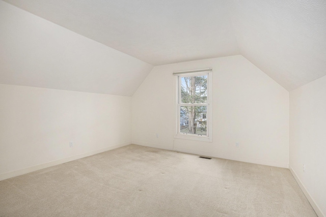 additional living space with baseboards, visible vents, lofted ceiling, and light carpet