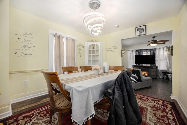 dining area with a lit fireplace, ceiling fan with notable chandelier, baseboards, and wood finished floors