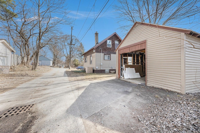 view of side of property featuring driveway, a chimney, a detached garage, and an outdoor structure