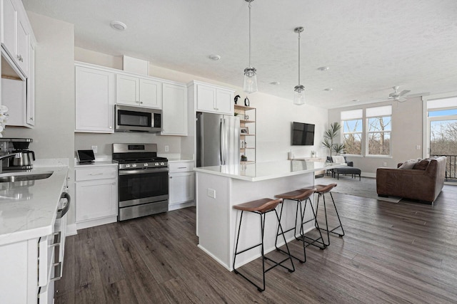 kitchen featuring a sink, white cabinets, appliances with stainless steel finishes, open floor plan, and a center island