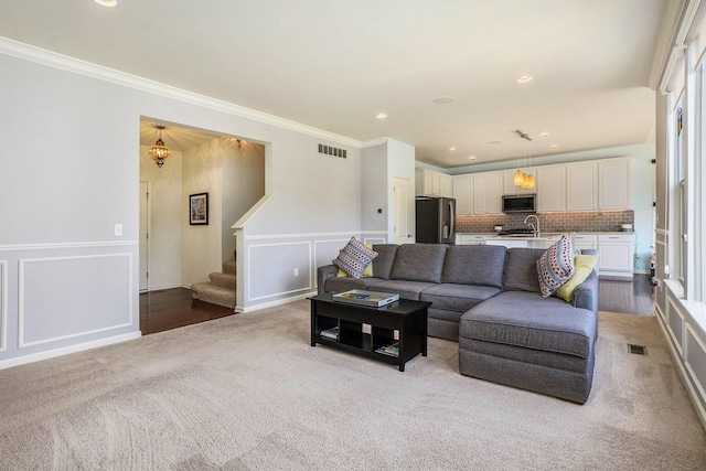 living area featuring stairway, visible vents, ornamental molding, and a decorative wall