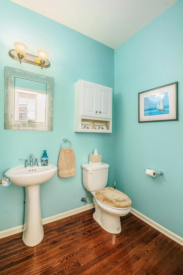 half bathroom featuring a sink, baseboards, toilet, and wood finished floors