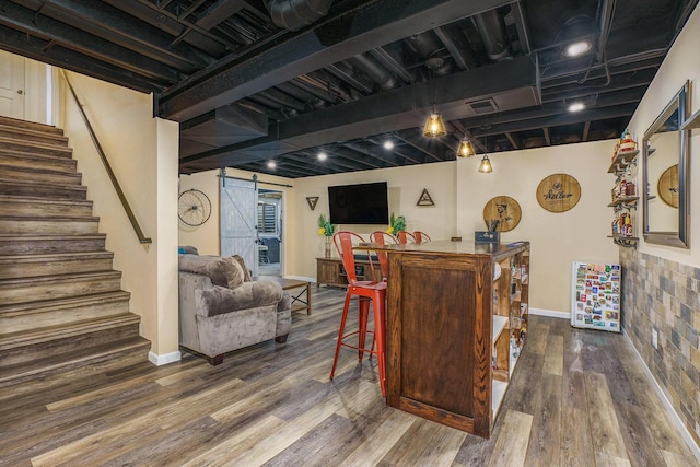 bar with a barn door, bar, wood finished floors, and stairway