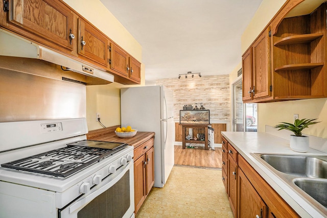 kitchen featuring brown cabinets, a sink, white appliances, wooden walls, and light countertops