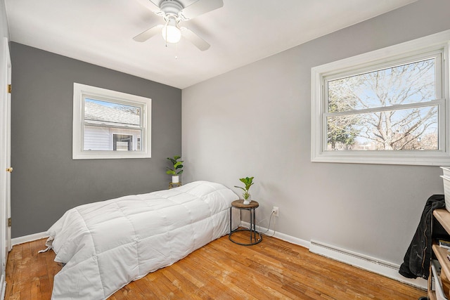 bedroom with a baseboard heating unit, baseboards, wood finished floors, and a ceiling fan