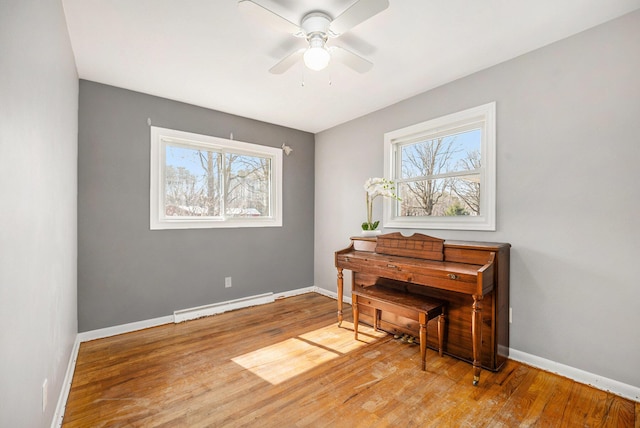 living area featuring a baseboard heating unit, wood finished floors, baseboards, and ceiling fan