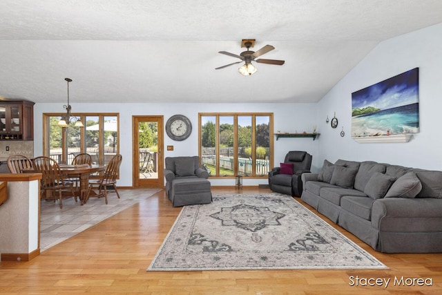 living room featuring ceiling fan with notable chandelier, a healthy amount of sunlight, light wood-style flooring, and vaulted ceiling