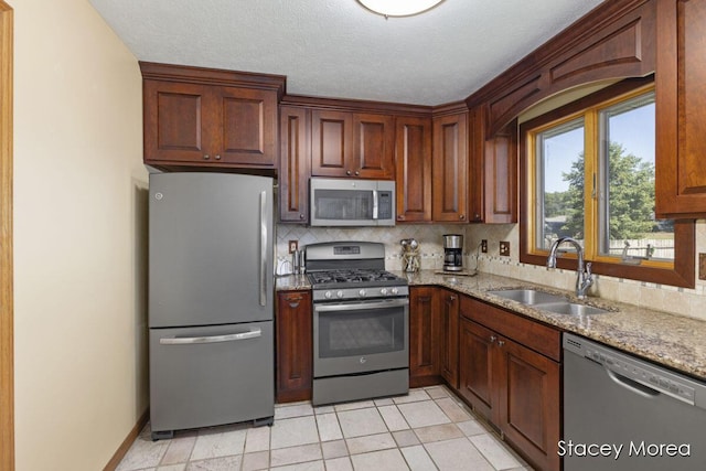 kitchen with a sink, backsplash, a textured ceiling, stainless steel appliances, and light stone countertops