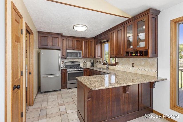 kitchen with a peninsula, a sink, stainless steel appliances, glass insert cabinets, and backsplash