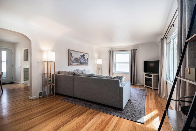 living area featuring arched walkways, light wood finished floors, and baseboards