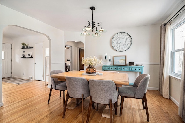 dining room featuring baseboards, an inviting chandelier, washer / clothes dryer, arched walkways, and light wood-style floors