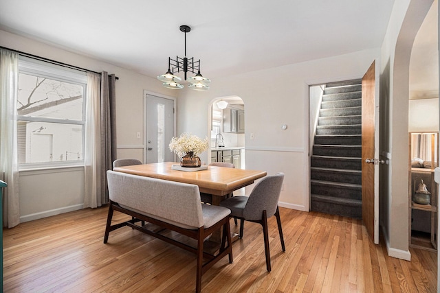 dining room featuring light wood-type flooring, stairway, arched walkways, and baseboards