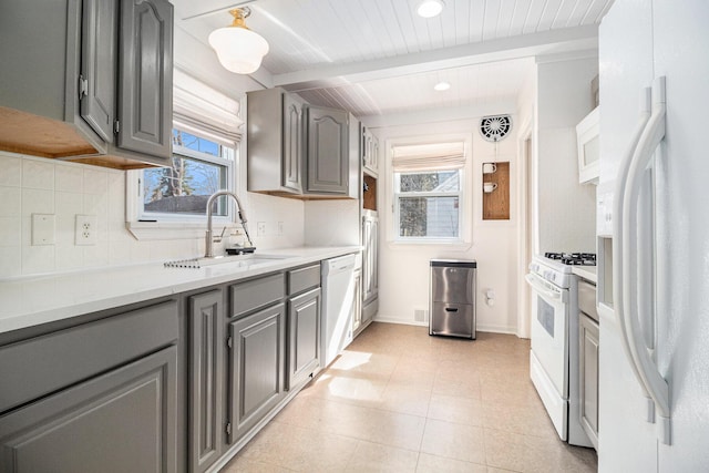 kitchen with beamed ceiling, gray cabinetry, a sink, plenty of natural light, and white appliances