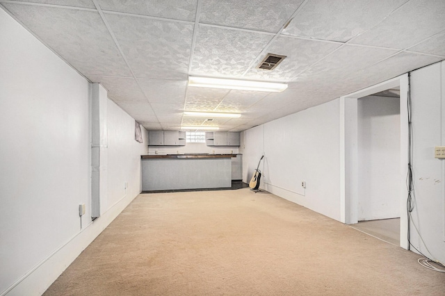 basement with a drop ceiling, visible vents, and light carpet