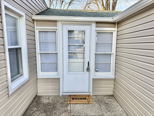 view of exterior entry featuring roof with shingles