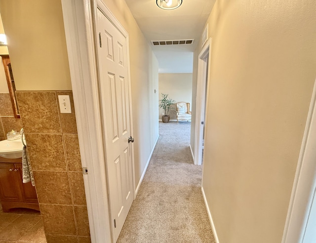 corridor featuring visible vents, light colored carpet, tile walls, and a sink