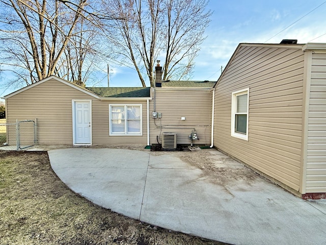 back of property with cooling unit, fence, a shingled roof, a chimney, and a patio area