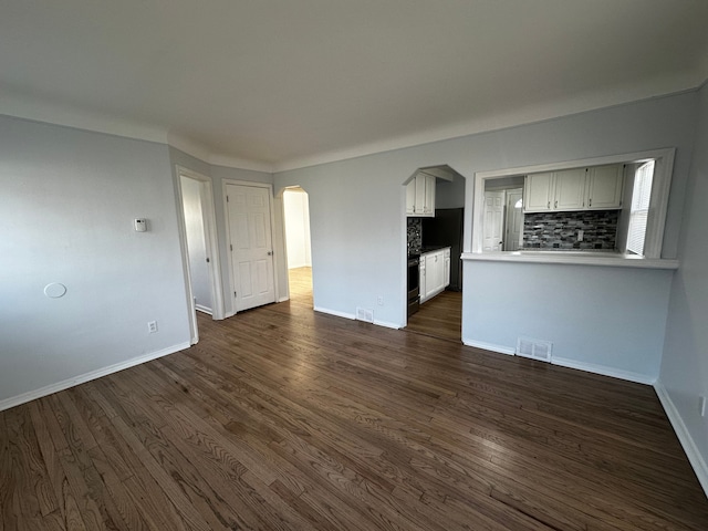 unfurnished living room featuring visible vents, arched walkways, baseboards, and dark wood finished floors