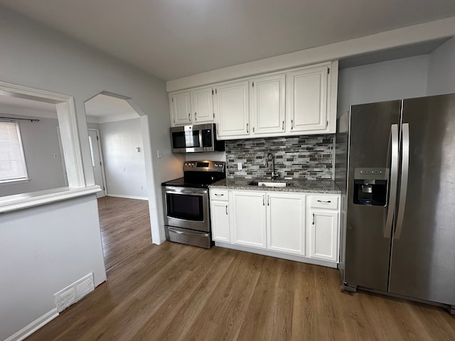 kitchen featuring visible vents, appliances with stainless steel finishes, arched walkways, white cabinetry, and a sink