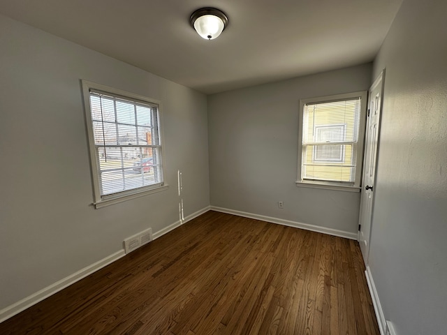 unfurnished room featuring plenty of natural light, baseboards, visible vents, and dark wood-style flooring