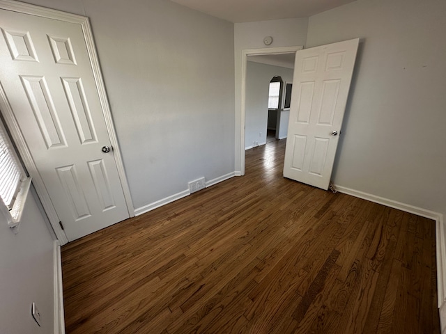 unfurnished bedroom featuring dark wood finished floors, visible vents, arched walkways, and baseboards