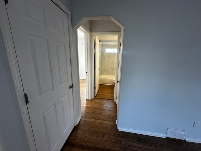 hall featuring arched walkways, visible vents, baseboards, and dark wood-style flooring