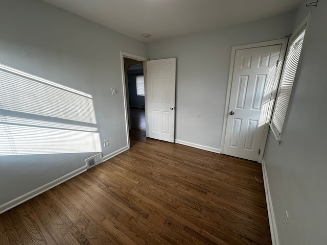 unfurnished bedroom with visible vents, dark wood-style floors, and baseboards