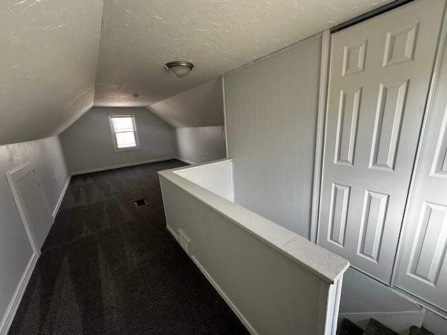 interior space featuring lofted ceiling, visible vents, dark carpet, and a textured ceiling