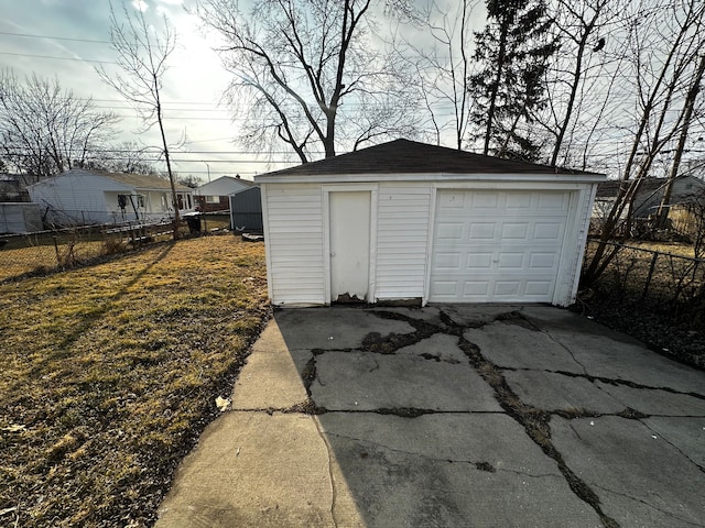 detached garage featuring concrete driveway and fence