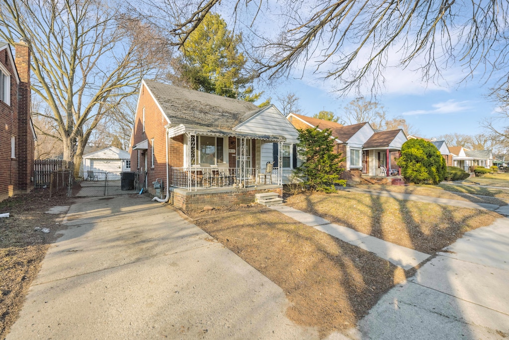 bungalow-style house with a gate, a porch, fence, a residential view, and brick siding