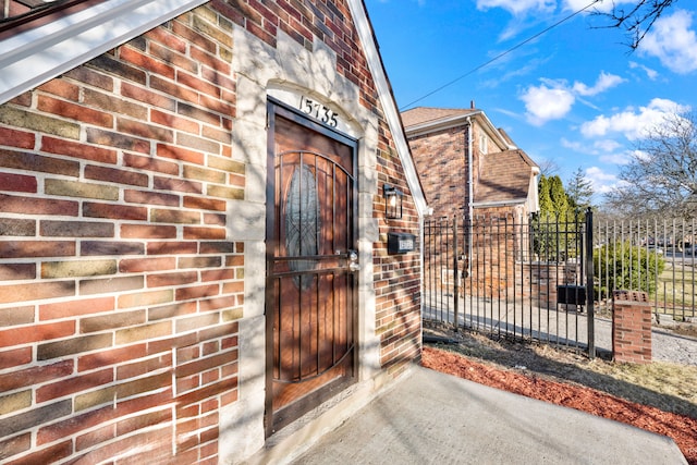 doorway to property featuring a gate, fence, brick siding, and a shingled roof