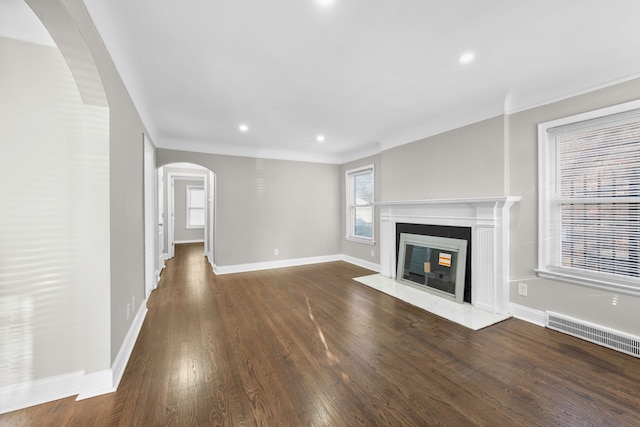 unfurnished living room with visible vents, wood finished floors, arched walkways, a premium fireplace, and baseboards