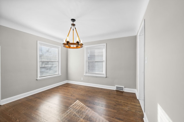 empty room with a notable chandelier, dark wood-style floors, visible vents, and baseboards