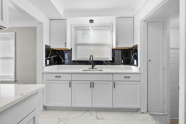 kitchen featuring a sink, tasteful backsplash, marble finish floor, and white cabinets