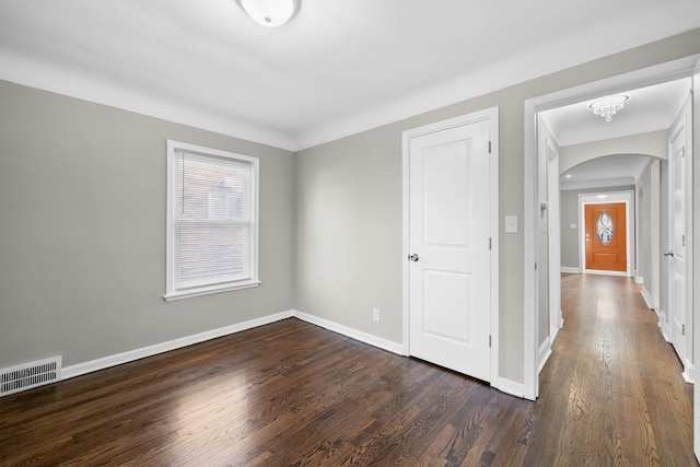 unfurnished bedroom with arched walkways, visible vents, baseboards, and dark wood-style floors