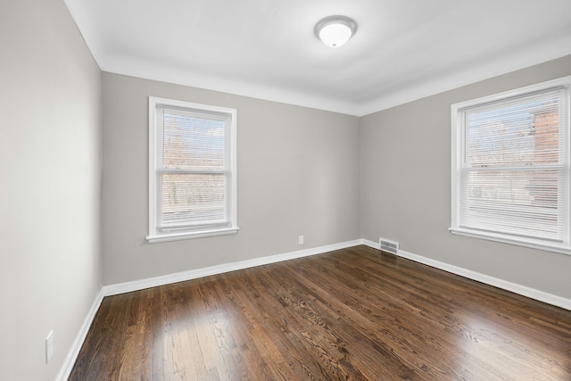 unfurnished room featuring dark wood-style floors, visible vents, and baseboards