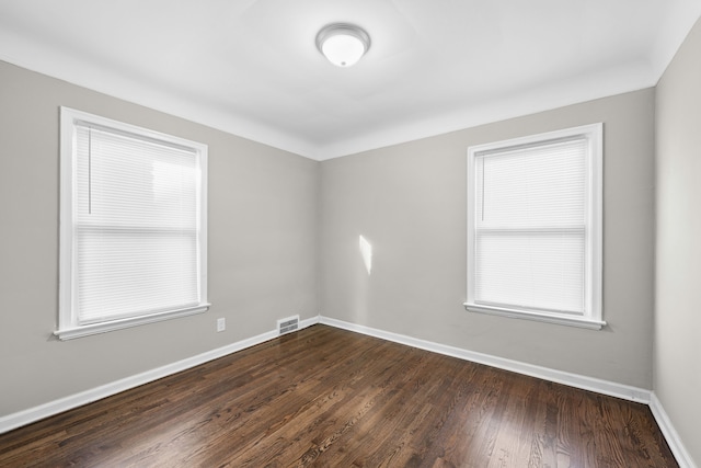 unfurnished room featuring visible vents, baseboards, and dark wood finished floors