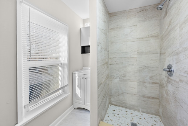 full bath featuring vanity, baseboards, and a tile shower