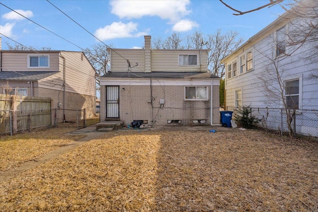 rear view of house with brick siding, a chimney, a fenced backyard, and roof with shingles