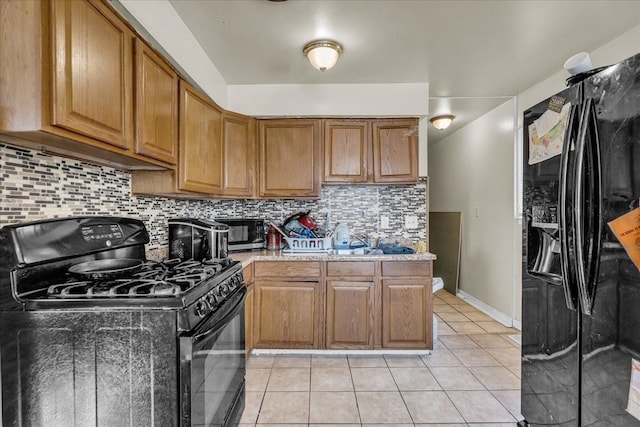 kitchen with light tile patterned floors, baseboards, black appliances, brown cabinets, and backsplash