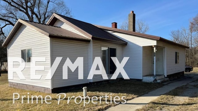 view of side of property with a yard, a chimney, and metal roof