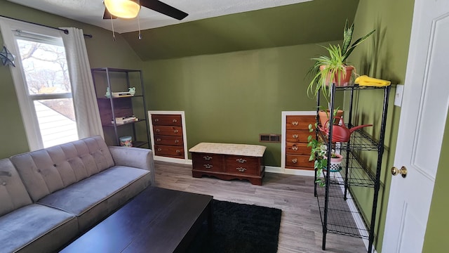 interior space with a ceiling fan, vaulted ceiling, wood finished floors, and visible vents