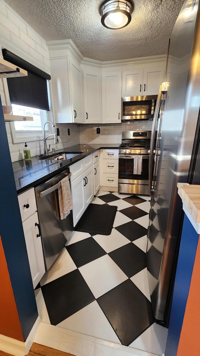 kitchen featuring dark countertops, a sink, white cabinets, appliances with stainless steel finishes, and tile patterned floors