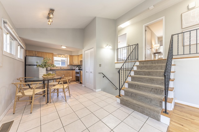 dining area featuring stairway, visible vents, baseboards, lofted ceiling, and light tile patterned flooring