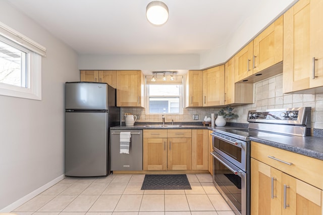 kitchen featuring tasteful backsplash, dark countertops, under cabinet range hood, appliances with stainless steel finishes, and a sink