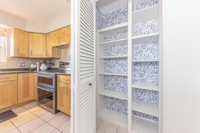 kitchen featuring light tile patterned floors, range with two ovens, light brown cabinetry, decorative backsplash, and dark countertops