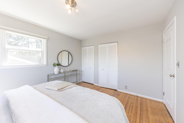 bedroom with multiple closets, baseboards, and wood finished floors