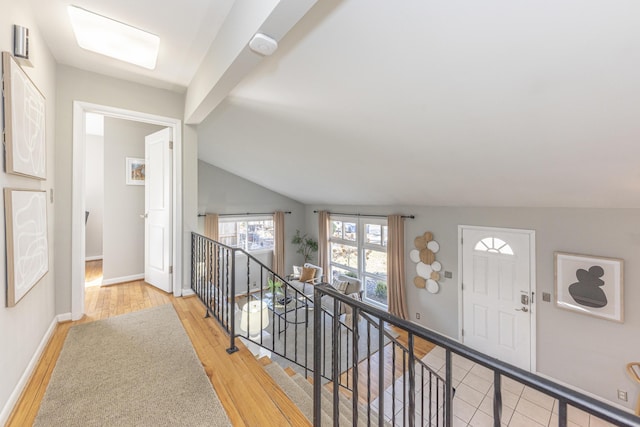 hallway featuring an upstairs landing, baseboards, light wood-style floors, and vaulted ceiling