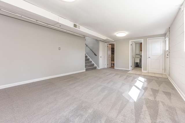 empty room featuring stairway, light colored carpet, visible vents, and baseboards